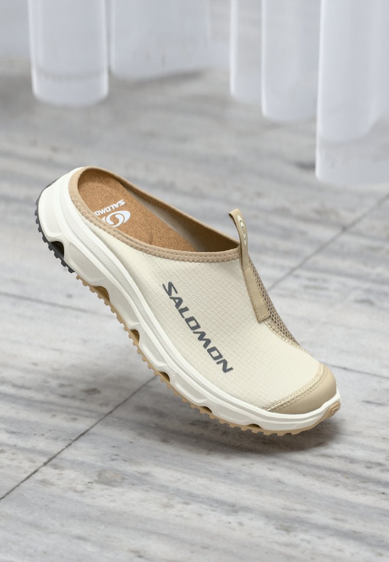 Beige slip-on sko med teksturert overdel, korkinnlegg, gummisåle og trykt "Salomon" logo. Har en bakre trekkstang.