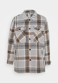 Camisa de manga larga a cuadros en tonos gris, blanco y marrón. Cuenta con dos bolsillos delanteros, cierre de botones y un tejido suave y texturizado.