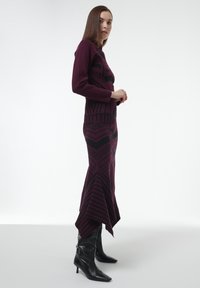 Conjunto de punto color burdeos con patrones geométricos angulares en negro, combinado con unas botas de tacón negro alto hasta la rodilla y un dobladillo asimétrico único.