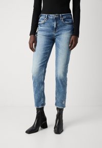Hellblaue Jeans aus Denim mit lockerer Passform, fünf Taschen, kontrastierenden Nähten und floralem Stickerei am Saum. Kombiniert mit schwarzen Knöchelstiefeln.