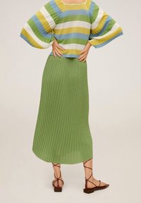 Top de punto a rayas y con relieve en azul, verde y amarillo. Mangas acampanadas y falda maxi verde con pliegues, combinada con sandalias planas marrones.