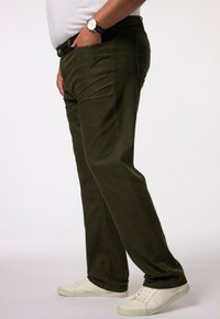 Pantalones cargo color caqui con un diseño de pierna recta, hechos de una mezcla de algodón, que presentan bolsillos laterales y una textura suave. Llevados con zapatillas blancas.
