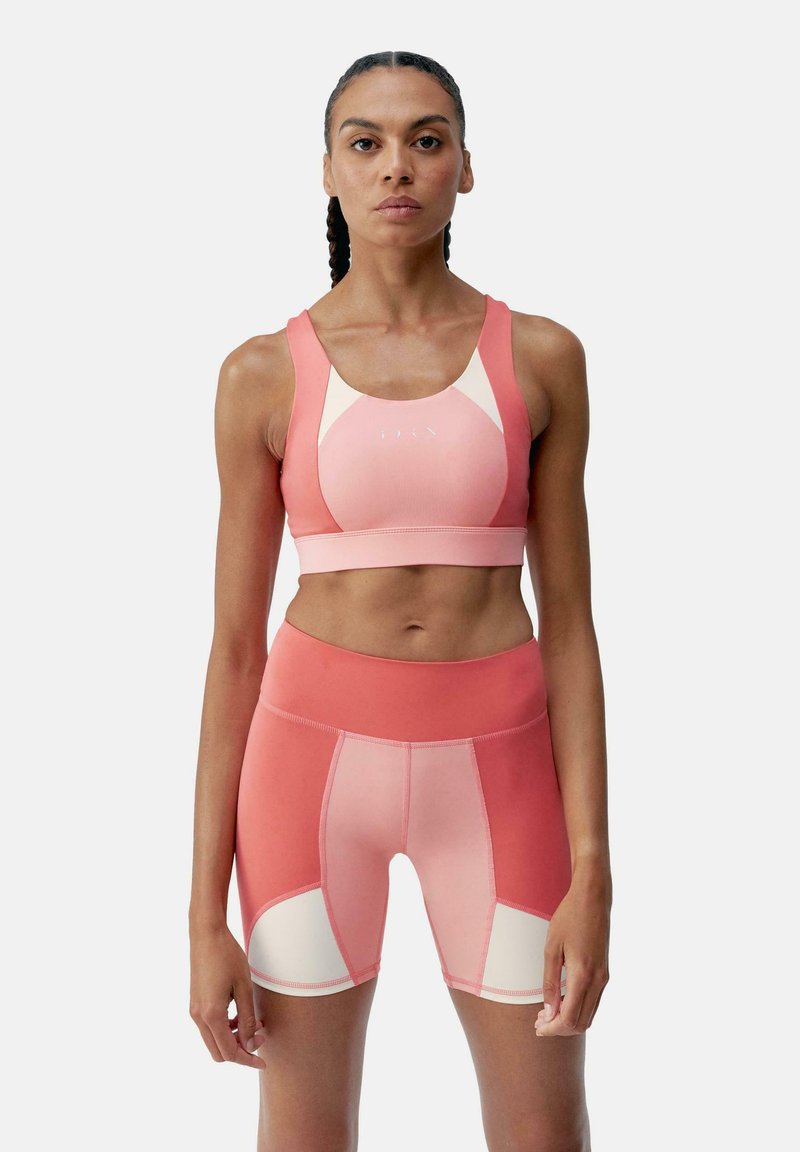 Sport bra and shorts set in gradient shades of pink. Smooth, stretchy fabric with contrasting cream panels and flat seams for comfort.