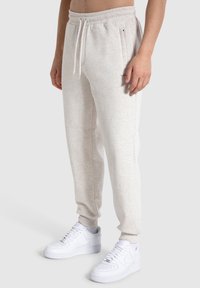 Hellgraue Sweatpants aus weichem Material, mit einem elastischen Bund und Kordelzug sowie Seitentaschen, kombiniert mit weißen Sneakers.