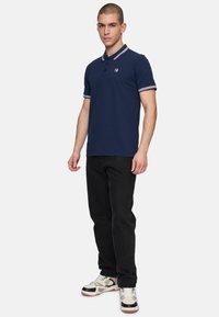 Marineblauwe polo met contrasterende kraag en mouwen, gecombineerd met zwarte jeans en meerkleurige sneakers. Slanke pasvorm.