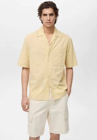 Korte mouwen, knoopsluiting shirt in zachtgeel met een textuurpatroon. Gekozen in combinatie met lichtbeige cargoshorts met zijzakken.