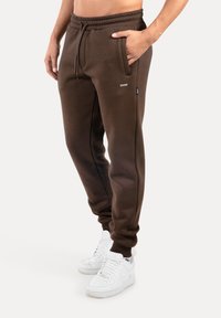 Brązowe spodnie dresowe wykonane z miękkiego materiału, z elastycznym pasem, bocznymi kieszeniami i dopasowanym krojem, zestawione z białymi trampkami.