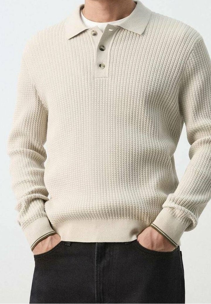 Homme portant un pull en maille côtelée crème avec col et patte à trois boutons, mains dans les poches, assorti à un pantalon noir.