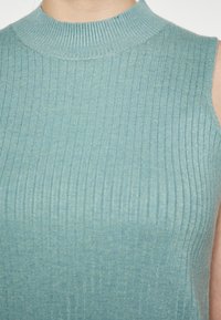 Mouwloze geribbelde top in licht teal, met een hoge hals en subtiele textuur. Het materiaal lijkt zacht en comfortabel met een aansluitende silhoutte.
