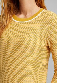 Gelbes Strickpullover mit einem strukturierten Wabenmuster, geripptem Rundhalsausschnitt und weißen Akzenten am Kragen. Klassische Passform.