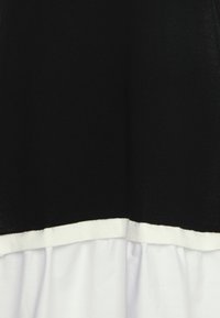Černobílé šaty s černou horní částí se strukturovaným pletením a bílým volánkovým spodkem, který vytváří vrstvený design.