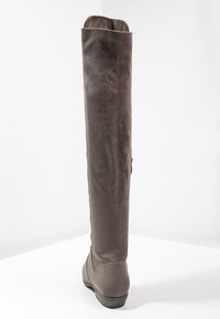Stivale al ginocchio in suede marrone con texture liscia, punta arrotondata e tacco basso. Presenta una silhouette aderente e nessun hardware visibile.