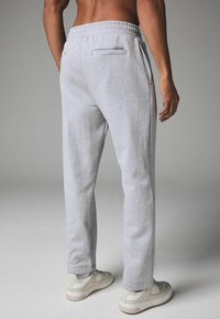 Helle graue Jogginghose mit tailliertem Schnitt, elastischem Bund und zwei Gesäßtaschen, getragen mit cremefarbenen Sportschuhen.