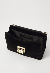 Pochette en velours noir avec un fermoir en métal doré, présentant un extérieur lisse et une doublure en tissu. L'étiquette affiche la marque "Furla".