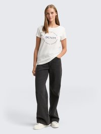 Camiseta blanca con estampado circular azul marino que dice "DENIM", combinada con pantalones de tiro alto de pierna ancha en negro y zapatillas blancas.