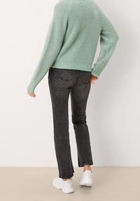 Maglione a maglia verde menta con vestibilità ampia e polsini a coste, abbinato a jeans neri slim e sneakers bianche. Texture morbida, design crop.