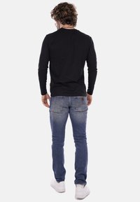 Maglietta nera a maniche lunghe, design aderente, abbinata a jeans in denim azzurro chiaro con leggeri segni di usura e due tasche posteriori. Sneaker bianche.