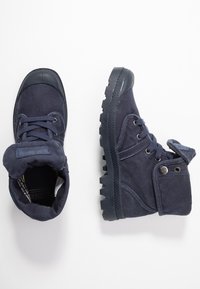 Botas de tobillo de tela azul marino con suelas de goma, punta redonda, cierre de cordones, cuello acolchado y botón lateral para ajuste regulable.
