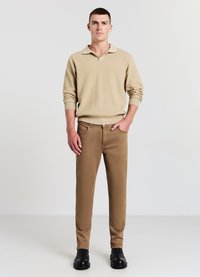 Beige Strickpullover mit Kragen, kombiniert mit braunen Slim-Fit-Hosen und schwarzen Ankle Boots. Glatte Texturen und klare Linien sind sichtbar.