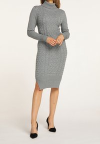 Robe en tricot grise avec un col roulé haut, présentant un motif en relief de torsades, des poignets et un ourlet côtelés, ainsi que des fentes latérales pour un détail supplémentaire.