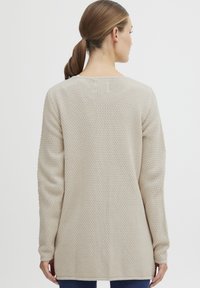 Beige pletený svetr s texturovaným vzorem, dlouhými rukávy a kulatým výstřihem, dosahující do poloviny boků.