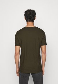 Camiseta de manga corta en color verde oliva, hecha de tejido suave, con cuello redondo y un corte relajado, que presenta una textura suave y un diseño sencillo.