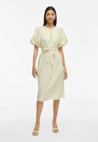 Blommigt tryckklänning i ljusbeige med puffärmar, knytning i midjan, knäppdetalj och rak kjol som går nedanför knäet. Mjuk textur.