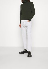 Zielony sweter z golfem, białe proste spodnie i czarne loafersy. Sweter ma miękką fakturę; spodnie charakteryzują się czystym designem.