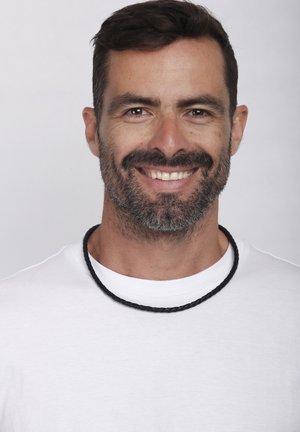 Schwarzer geflochtener Halsreifen, der über einem weißen T-Shirt getragen wird, mit einem Nahaufnahme-Porträt vor einem neutralen Hintergrund und einem lächelnden Gesichtsausdruck.