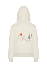 Beige hoodie with a hood, featuring a desert scene graphic in black and an orange sun. Text reads "ESCAPE AND DISCOVER THE WORLD."