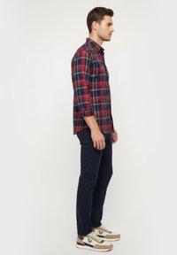 Camisa de cuadros roja y azul marino de manga larga, combinada con pantalones oscuros y zapatillas multicolores. Tejido suave, corte casual.