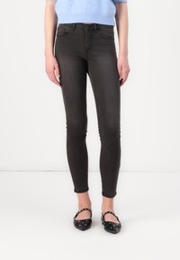 Jeans ajustados negros con una forma ceñida, diseño de cinco bolsillos y un leve desgaste. Combinados con bailarinas negras que cuentan con herrajes decorativos.
