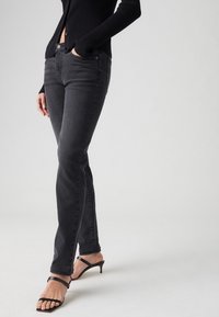 Jeans de mezclilla negra con corte ajustado, que incluyen bolsillos frontales, cremallera y un ligero desvanecimiento. Combinados con tacones negros con tiras.