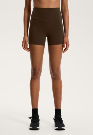 Bruna högmidjade shorts med en figursydd design. Slät textur, knäslå och en sömlös midja för komfort. Matchas med svarta sneakers.