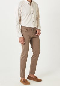 Camisa de botones beige claro, pantalones marrones de corte slim y zapatos de mocasín marrones. Diseño sencillo sin patrones ni acentos visibles.