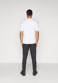 Λευκό πουκάμισο με κοντά μανίκια και μαύρες λεπτομέρειες, σε συνδυασμό με μαύρο παντελόνι που έχει ροζ ραφές και φερμουάρ στους αστραγάλους. Ολοκληρώνεται με αθλητικά παπούτσια.