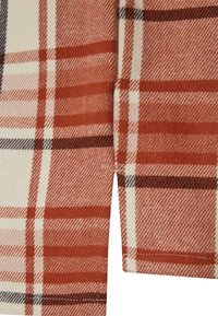 Tkanina tkaná v odstínech oranžové a krémové, s kostkovaným vzorem a černými akcenty. Měkká textura, částečně složená.