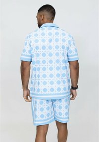 Ensemble composé d'une chemise à manches courtes à motif bleu et d'un short, mettant en avant des motifs géométriques et des accents blancs contrastants. Tissu doux avec une légère texture.