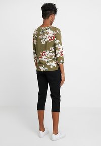 Haut floral vert olive avec des manches ¾, doté d'un dos en trou de serrure. Associé à un pantalon capri noir ajusté et des baskets blanches.