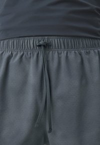 Shorts de sport gris en tissu texturé et perforé. Dotés d'une taille élastique et d'un cordon de serrage noué pour un ajustement optimal.