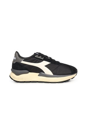 Zapatilla deportiva baja en negro y gris con detalle de logo blanco, suela gruesa beige y cordones negros, vista desde el lateral exterior sobre fondo blanco.