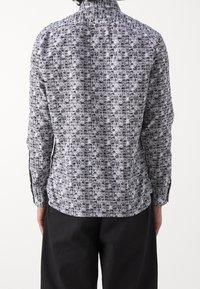 Långärmad skjorta med svartvitt geometriskt mönster. Tillverkad i bomull, med krage och knappar samt slitsar i sidorna vid fållen.