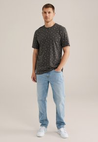 Grå kortærmet t-shirt med et diskret hvidt mønster, parret med lyseblå denim jeans og hvide sneakers. Blødt bomuldsstof.