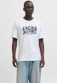 Balts kokvilnas T-krekls ar daudzkrāsainu grafisku tekstu "JACK & JONES Essentials" krūšu daļā. Tam ir īsas piedurknes un brīvs piegriezums.