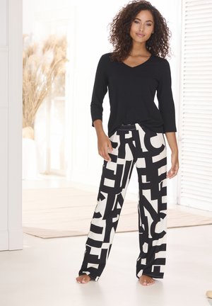 Schwarzes Langarm-V-Ausschnitt-Oberteil kombiniert mit weißen Hosen, die auffällige schwarze Typografie aufweisen. Weiches Material mit lockerer Passform und weitem Bein.