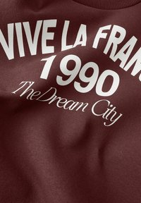 Felpa bordeaux con testo bianco audace: "VIVE LA FRANCE 1990 The Dream City", con una superficie liscia e texturizzata e design a girocollo.