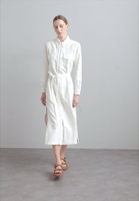 Balta, mygtukais suknelė su dviem krūtinės kišenėmis, diržu, šoninėmis skeltukais ir ilguoju rankovėmis, pagaminta iš minkštos, lengvos medžiagos.