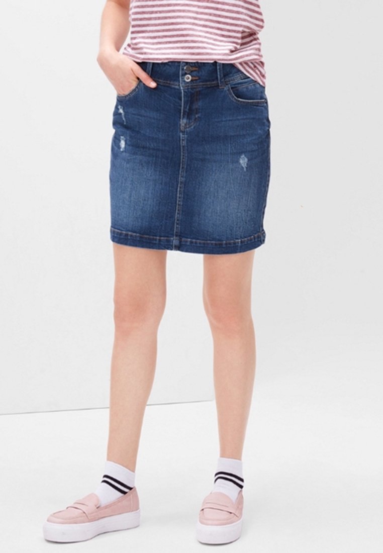 Femme portant une jupe en jean bleue avec des détails usés, un chemisier rayé, des chaussettes blanches à rayures noires et des mocassins compensés roses.