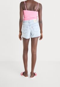 Pantalones cortos de mezclilla azul claro con un dobladillo deshilachado, dos bolsillos traseros y una etiqueta de marca. Combinados con una camiseta ajustada rosa y sandalias.