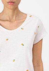White short-sleeve T-shirt featuring colorful embroidered oranges and green leaves in a scattered pattern. V-neck design. Soft texture.